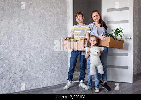 La famiglia si sposta in un nuovo appartamento, una bambina corre nella porta, tenendo scatole di cartone sullo sfondo. Madre con suo figlio e figlia Foto Stock