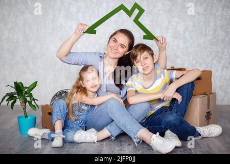 Una madre con suo figlio e sua figlia si sposta in un nuovo appartamento con le cose in scatole di cartone. La famiglia crea un tetto che promette eccellente Foto Stock