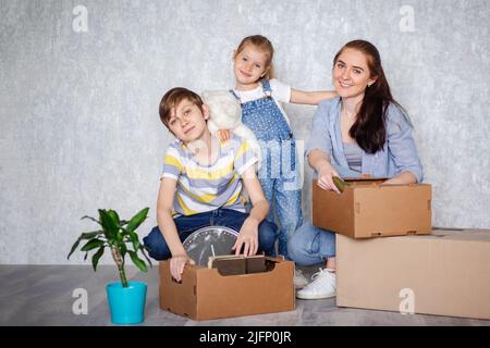 Una madre con suo figlio e sua figlia si sposta in un nuovo appartamento con le cose in scatole di cartone. La famiglia crea un tetto che promette eccellente Foto Stock