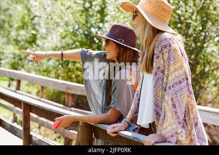 Così tanto da vedere quando non si siede a casa. Scatto di due giovani donne in piedi su un ponte e puntando durante una vacanza estiva. Foto Stock