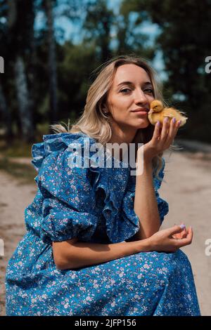 Bella giovane bionda in un abito blu nel bosco con anatroccoli Foto Stock