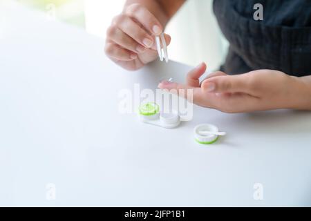 Donna mette la lente a contatto sul suo indice con pinzette. C'è un contenitore per lenti nelle vicinanze. Primo piano, vista laterale, banner, spazio di copia Foto Stock