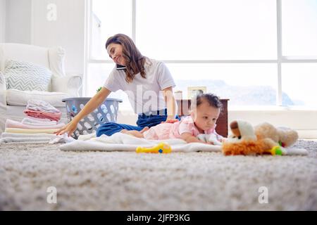 Rimanere forte per i miei figli è più difficile di quanto sembri. Scatto di una madre che si piega vestiti mentre il suo bambino gioca nella lounge. Foto Stock