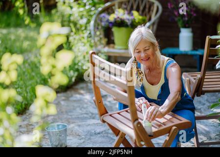 Donna anziana pulizia e ristrutturazione di mobili da giardino e preparare il giardino per l'estate Foto Stock