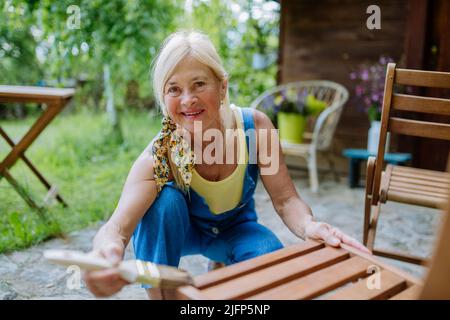 Donna anziana pulizia e ristrutturazione di mobili da giardino e preparare il giardino per l'estate Foto Stock