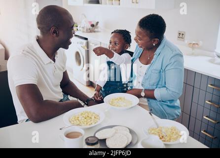 Non possiamo ottenere abbastanza delle sue guance chubby carine. Scatto di una giovane famiglia felice che si lega mentre mangiano la colazione nella cucina a casa. Foto Stock