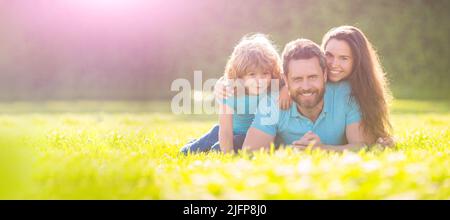 Giornata in famiglia. Bandiera di famiglia felice giacente sull'erba. Madre e padre giovani con figlio nel parco che riposa insieme sull'erba verde. Foto Stock