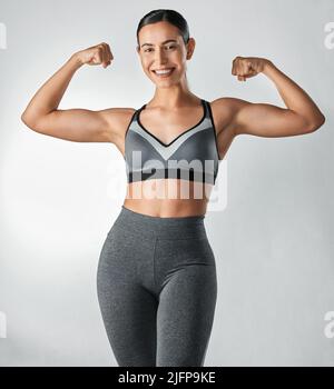 Non abbiate paura di mostrarlo. Ritratto da studio di una giovane donna sportiva che flette le braccia su uno sfondo grigio. Foto Stock