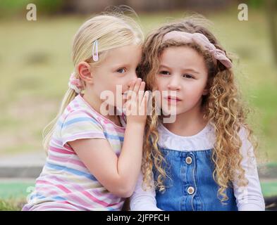 Non dire a nessuno che ti ho detto. Scatto di una bambina che sussurra nell'orecchio degli amici. Foto Stock