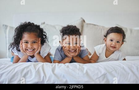 Fratelli e sorelle sono vicini come mani e piedi. Colpo di tre fratelli che si trovano insieme a letto. Foto Stock