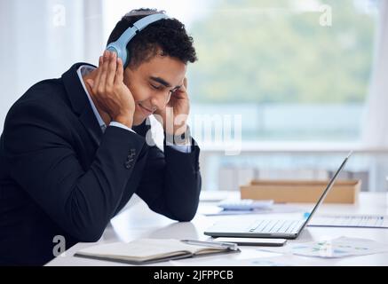 Perdersi nella musica mentre lavora. Scatto di un giovane uomo d'affari che indossa le cuffie mentre lavora in ufficio. Foto Stock