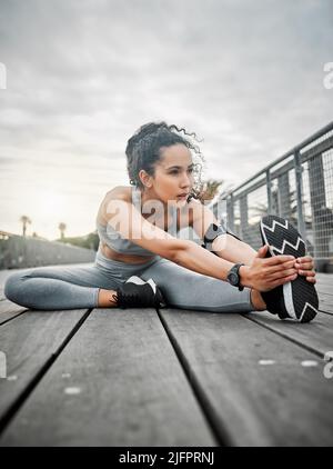 Riscaldare quelle gambe. Scatto a tutta lunghezza di una giovane atleta attraente che si riscalda prima della sua mattina correre fuori. Foto Stock