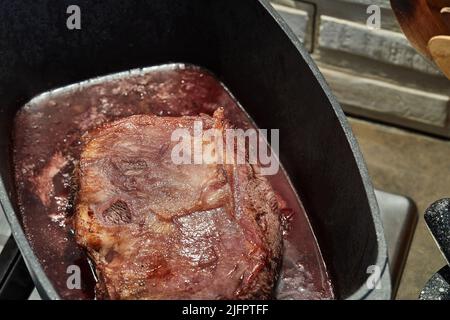 Pezzo di carne è fritto con cipolle in salsa di vino in padella rettangolare sul fuoco su stufa a gas Foto Stock