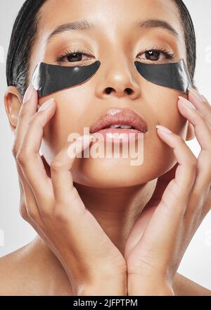 Infuso con i migliori ingredienti per una pelle più luminosa. Ritratto di studio di una giovane donna attraente indossando sotto le macchie degli occhi su uno sfondo grigio. Foto Stock