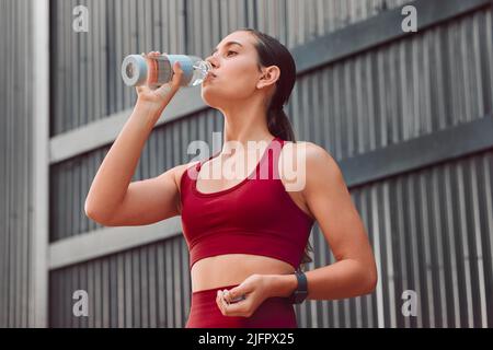 Idratazione. Scatto corto di una giovane atleta attraente acqua potabile mentre corre all'aperto. Foto Stock