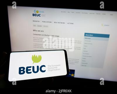 Persona che tiene uno smartphone con il logo di Bureau Europeen des Unions de Consommateurs (BEUC) sullo schermo di fronte al sito web. Mettere a fuoco sul display del telefono. Foto Stock