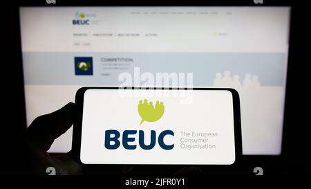 Persona che tiene il cellulare con il logo di Bureau Europeen des Unions de Consommateurs (BEUC) sullo schermo di fronte alla pagina web. Mettere a fuoco sul display del telefono. Foto Stock