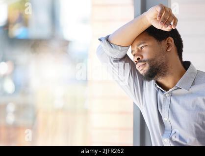 Troppo da fare, troppo da stress. Shot di un giovane uomo d'affari che guarda stressato mentre si alza in piedi in una finestra in un ufficio. Foto Stock