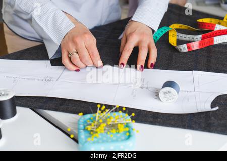 Giovane sneamstress che si aggraffa il modello di carta sul tessuto. Donna su misura sews vestiti con le proprie mani Foto Stock