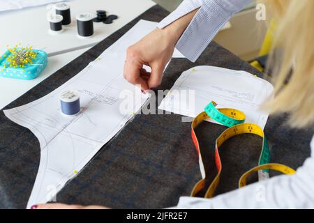 Il dressmaker contrassegna un pezzo di tessuto con gesso in base al modello di carta. Lavoro di sarto, utensili per cucire Foto Stock