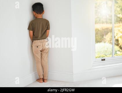 Ci sono modi diversi per disciplinare un bambino. Scatto di un ragazzino in piedi in un angolo a casa. Foto Stock