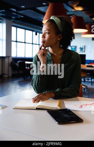 Giovane donna d'affari afroamericana con mano sul mento in ufficio creativo Foto Stock