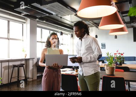 Giovane uomo d'affari e donna d'affari multirazziale che discute su laptop in ufficio creativo Foto Stock