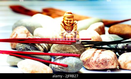 Statuette di un monaco buddista tra incenso e varie pietre Foto Stock