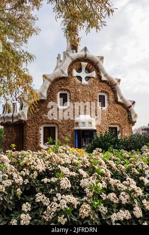 Foto verticale del Pavillon di Porter's Lodge a Park Güell. Landmark Catalano con Bush albero e fiore in un giorno nuvoloso a Barcellona. Foto Stock