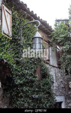 Scenario romantico con un edificio medievale in pietra e coperto di edera, che hanno all'ingresso una vecchia lanterna in ferro battuto Foto Stock