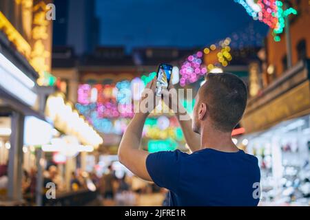 Vista posteriore dell'uomo mentre si scattano foto con il telefono cellulare su strade colorate. Turista a Chinetown in Singapore. Foto Stock