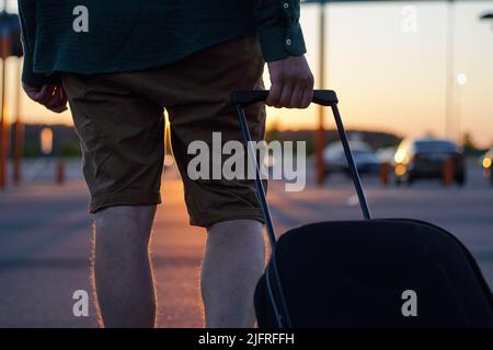 Il viaggiatore giovane cammina con la valigia di trasporto in aeroporto. I passeggeri viaggiano nel fine settimana. Concetto di viaggio aereo. Foto Stock