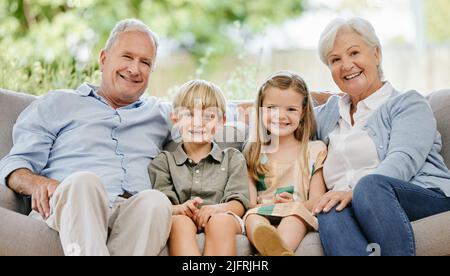 Ritratto di una famiglia affettuosa di quattro seduti comodamente sul loro divano nel soggiorno di casa. Nonna, nonno, nipote e. Foto Stock