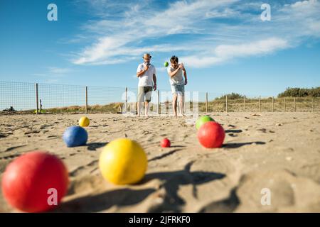I turisti giocano un gioco attivo, petanque su una spiaggia sabbiosa vicino al mare - Gruppo di giovani che giocano a bocce all'aperto in vacanza al mare Foto Stock