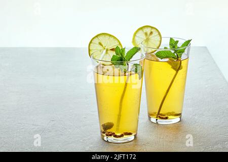 Due tazze di vetro di tè Kombucha fermentato fatto in casa sono decorate con menta e limone su un tavolo di cemento grigio chiaro. Bevanda a basso contenuto di alcol gassato su un Foto Stock