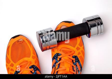 Sneakers indossate e buie con le dita dei piedi sporgenti e un mumbell in metallo caduto sul piede, isolato su uno sfondo bianco. Esercitazioni quotidiane di sicurezza e di usura Foto Stock