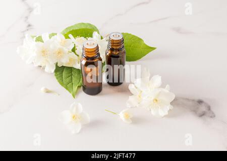 due flaconi per uso medico con una pipetta con olio essenziale di gelsomino su sfondo di marmo bianco e fragranti fiori di gelsomino. spa, aromaterapia, cura del corpo Foto Stock