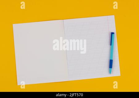 Quaderno scolastico su sfondo giallo con spazio di copia per testo e penna blu. Torna a scuola. Foglio bianco con linee oblique nel libro degli esercizi Foto Stock