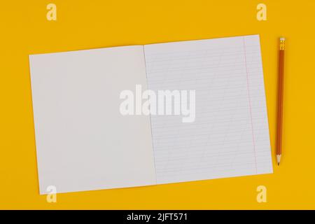 Quaderno scolastico su sfondo giallo con spazio di copia per testo e matita. Torna a scuola. Foglio bianco con linee oblique nel libro degli esercizi. Foto Stock