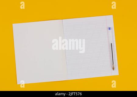 Quaderno scolastico su sfondo giallo con spazio di copia per testo e penna trasparente. Torna a scuola. Foglio bianco di carta con linee oblique in exerci Foto Stock