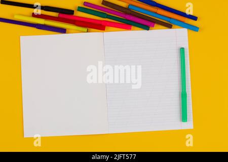 Quaderno scolastico su sfondo giallo con spazio di copia per il testo, pennarelli colorati. Torna a scuola. Foglio bianco di carta con linee oblique in esercizio Foto Stock