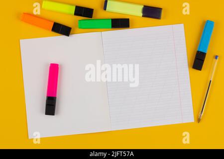 Quaderno scolastico su sfondo giallo con spazio di copia per testo, pennarelli colorati e penna. Torna a scuola. Foglio bianco con linee oblique in Foto Stock