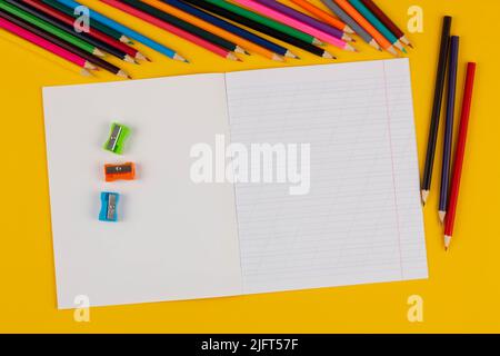 Quaderno scolastico su sfondo giallo con testo dello spazio di copia, matite colorate, pennarelli a matita. Torna a scuola. Foglio bianco con obliquo Foto Stock