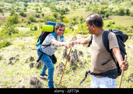 Middled Man aiutare il suo amico per arrampicarsi in collina durante le escursioni - concetto di sostegno, amicizia e attività ricreative. Foto Stock