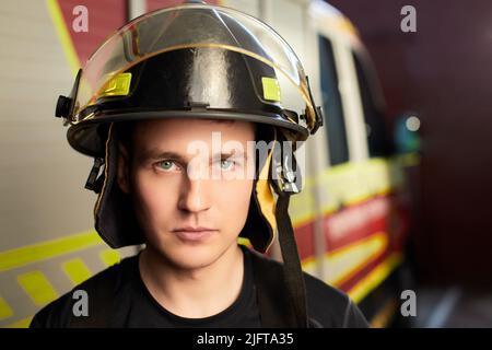 Vigile del fuoco in uniforme e casco in piedi dietro al camion del fuoco Foto Stock