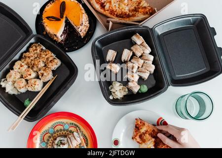 Tavolo da festa con cibo da togliere in confezione di plastica. Pizza, sushi panini e torta foto per menu. Consegna di cibo Foto Stock