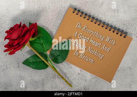 Citazione motivazionale sul libro marrone della nota con rose rosse - faccia tutto con un buon cuore e non si aspetti niente in cambio. Foto Stock