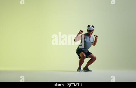 Uomo maturo che solleva un barbell virtuale utilizzando un paio di controller di gioco. Atletico uomo anziano che fa gli esercizi di sollevamento pesi nella realtà virtuale. Senior Foto Stock