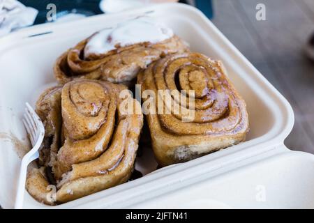 Grandi rotoli di cannella freschi e caldi in una scatola da andare da una panetteria Foto Stock