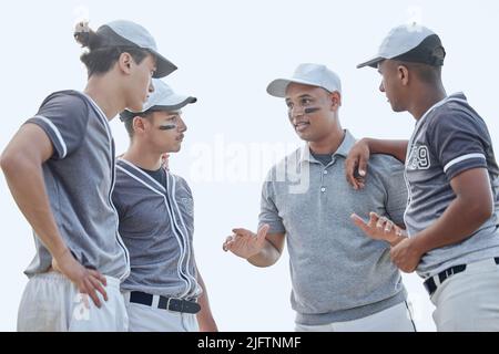 Allenatore di baseball da sotto che dà il pep talk della partita e la strategia di pianificazione del gioco con il gruppo di giocatori in huddle sul campo sportivo fuori. Formatore Foto Stock